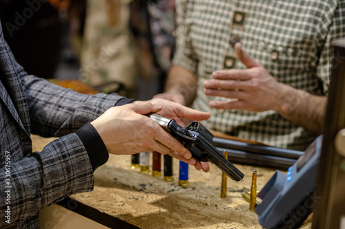 close-up photo of men using and inspecting gun in store. salesman explain how to use it, customer hold it in hands