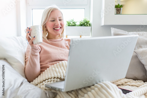 Happy casual beautiful woman working on a laptop laying on the bed in the house. Freelancer woman working on her laptop at home