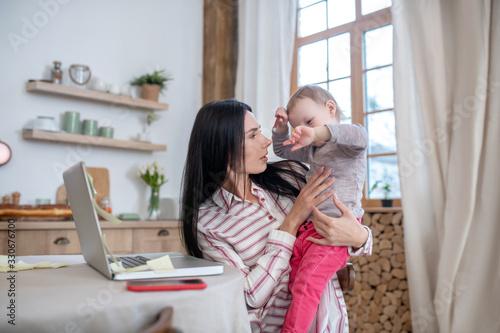 Young mom holding baby, distracted from work