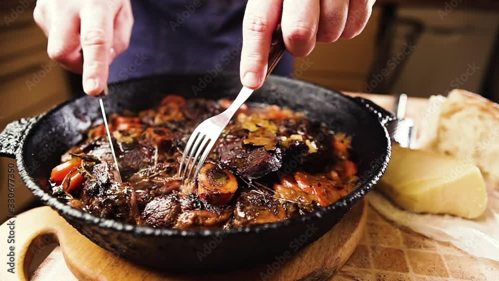 Man cuts a piece of beef, demonstrating cooked ossobuco. Traditional Italian food.