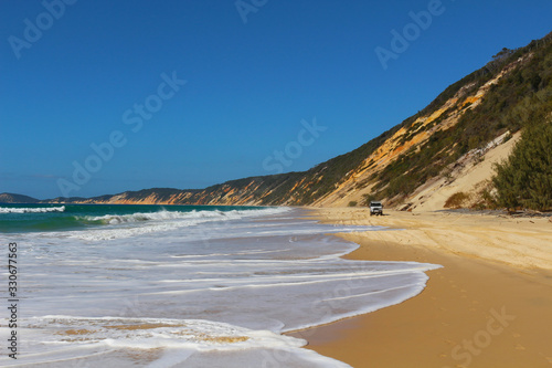 Beach along the coloured sands cliffs with rising tide and 4WD car in Rainbow Beach, Queensland, Australia