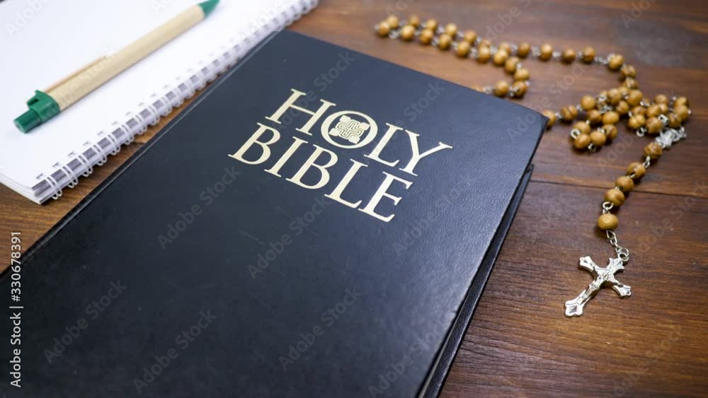 Holy Bible with beads with crucifix on brown wood table background. Green pen with open paper notebook. Study of Holy Scripture and religion concept Holy Bible with beads with crucifix on brown wood table background. Green pen with open paper notebook. Study of Holy Scripture and religion concept