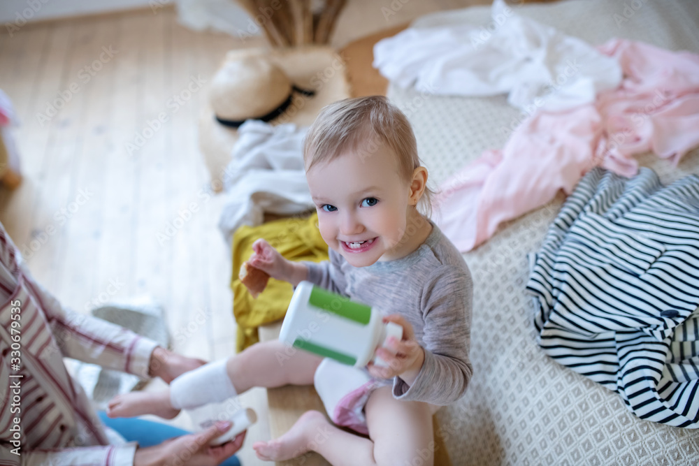 Fototapeta premium Baby holding medicine bottle with bandage on her leg, smiling