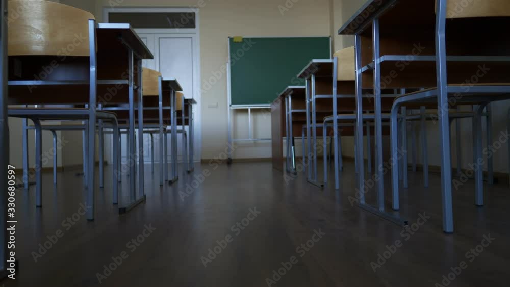 empty classroom during a break or vacation at school, university, institute, slow motion towards green blackboard, between two rows of desks