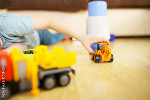 Little boy playing with toy excavator on wooden floor. 