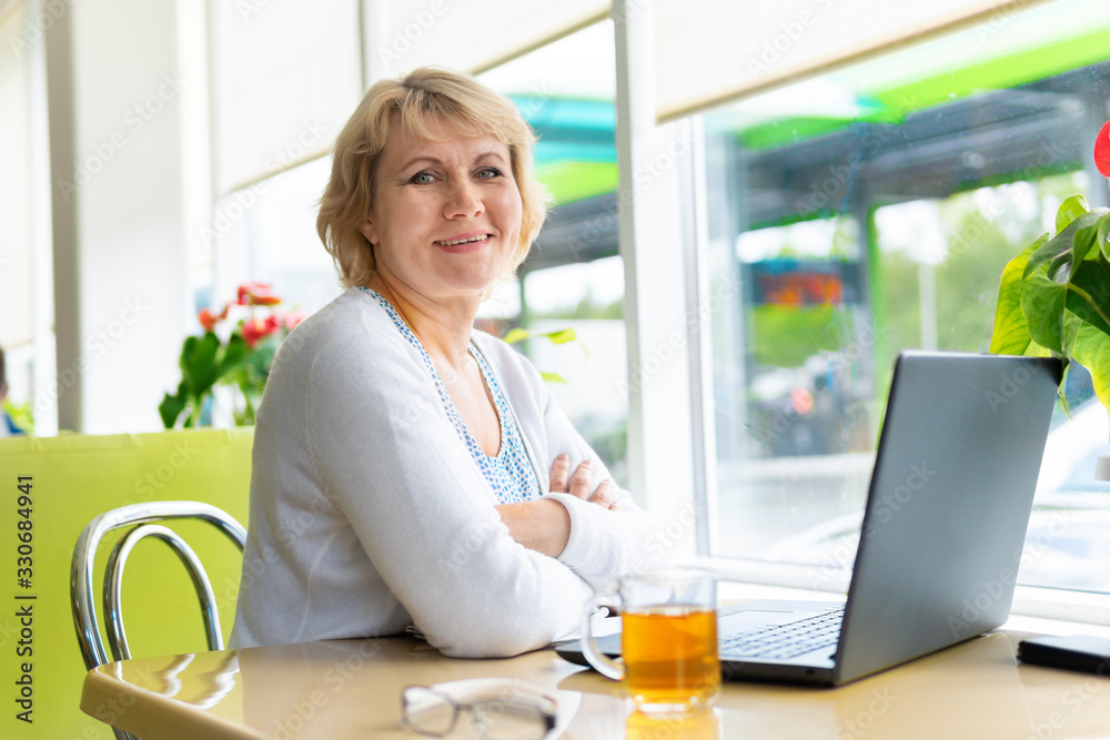 A woman with a laptop is working at a table near the window. A woman with a laptop is working at a table near the window.