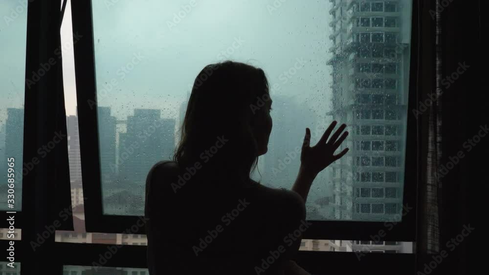 Silhouette sad loneliness woman touch glass window at rain day on city view background