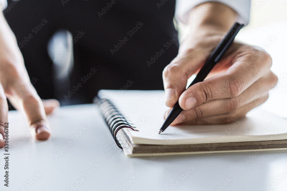 Man writes with a pen in diary in a sunny office, business and education concept. Close up Man writes with a pen in diary in a sunny office, business and education concept. Close up