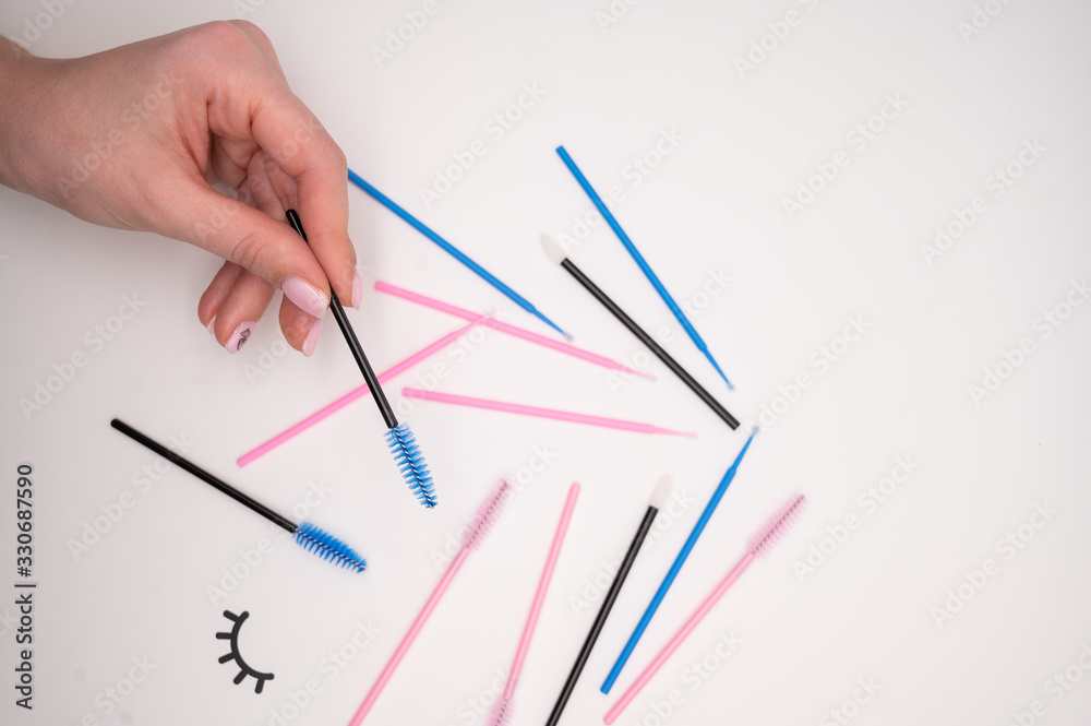 Top view of flatlay from eyelash extension tools. Female hand holds colored brushes for combing cilia. Top view of flatlay from eyelash extension tools. Female hand holds colored brushes for combing cilia.