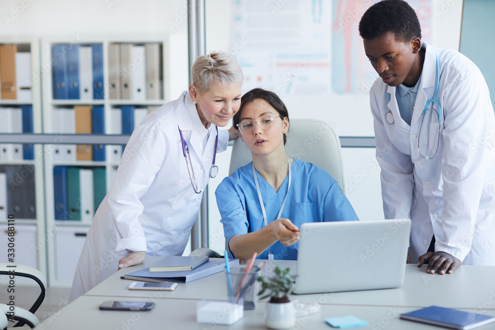 Multi-ethnic group of doctors using laptop while working on medical project together, copy space Multi-ethnic group of doctors using laptop while working on medical project together, copy space