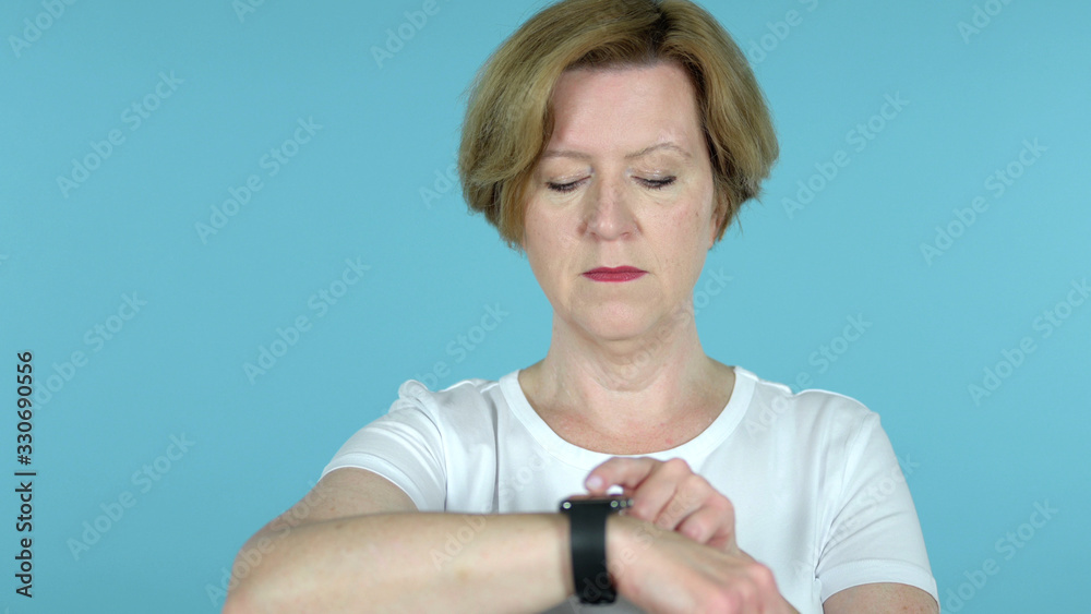 The Senior Woman Using Smartwatch Isolated on blue Background The Senior Woman Using Smartwatch Isolated on blue Background