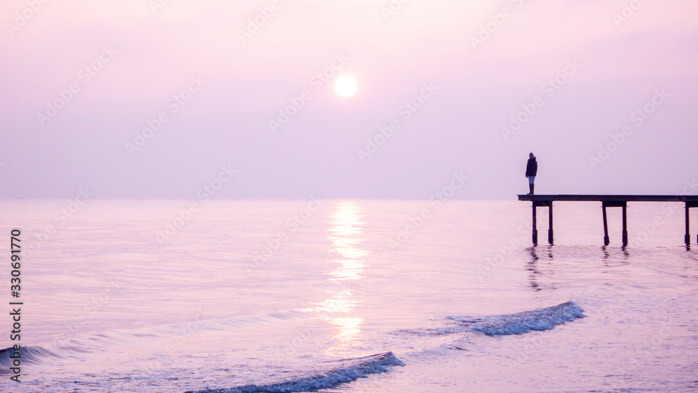Fototapeta premium Girl standing on a pier in sunset