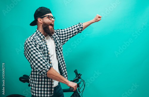 Portrait of hipster guy with green bicycle wearing white t-shirt and plaid shirt isolated over blue background.