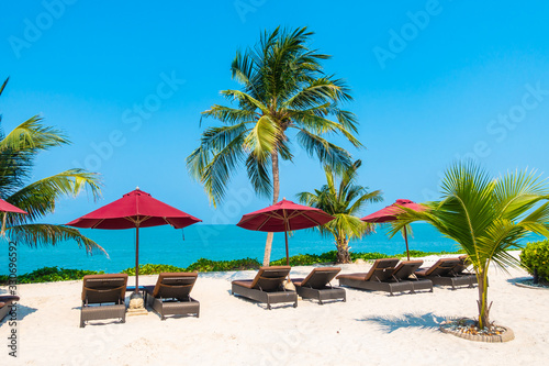 Beautiful tropical beach sea ocean with umbrella and chair around coconut palm tree on blue sky © siraphol