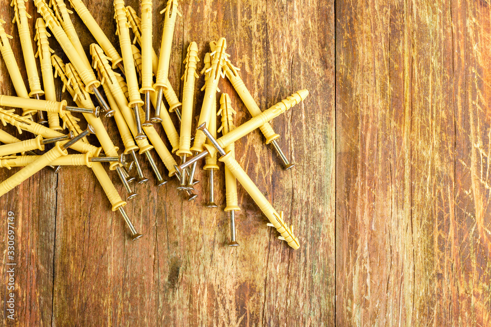 Pile of plastic dowels with metal screws lie in a row on a scratched wooden table. Home repair concept. Copy space for text.