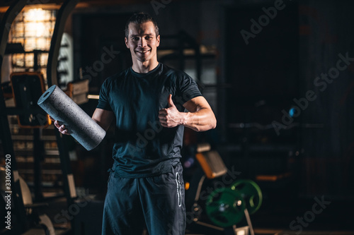 young cheerful personal trainer in gym and with fit roller