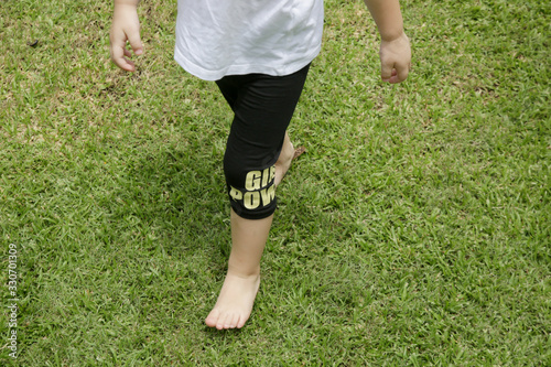 Child running barefoot on green grass. Walking barefoot can help develop muscles and ligaments in the foot, and strengthen the foot's arch and it is extremely beneficial for their motor development.