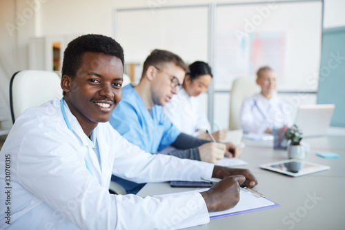 Portrait of young African-American doctor smiling at camera during medical council or conference in clinic, copy space