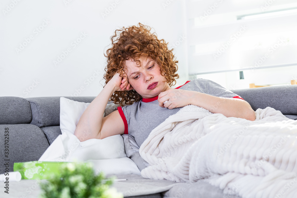Weak woman, wearing casual clothes is sitting on a sofa and taking a pill. Sick day at home. Young woman has common cold. Sickness, seasonal virus problem concept. Weak woman, wearing casual clothes is sitting on a sofa and taking a pill. Sick day at home. Young woman has common cold. Sickness, seasonal virus problem concept.