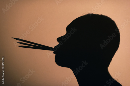 Shadow silhouette on a wall of a profile of a creative man thinking and holding three pencils in his mouth.