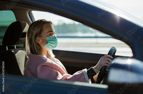 Woman in protective mask driving a car on road. Safe traveling.