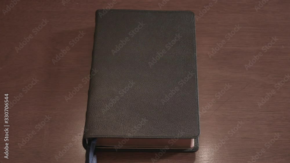 Hand opens a leather-bound holy Bible book sitting on a wood table Hand opens a leather-bound holy Bible book sitting on a wood table