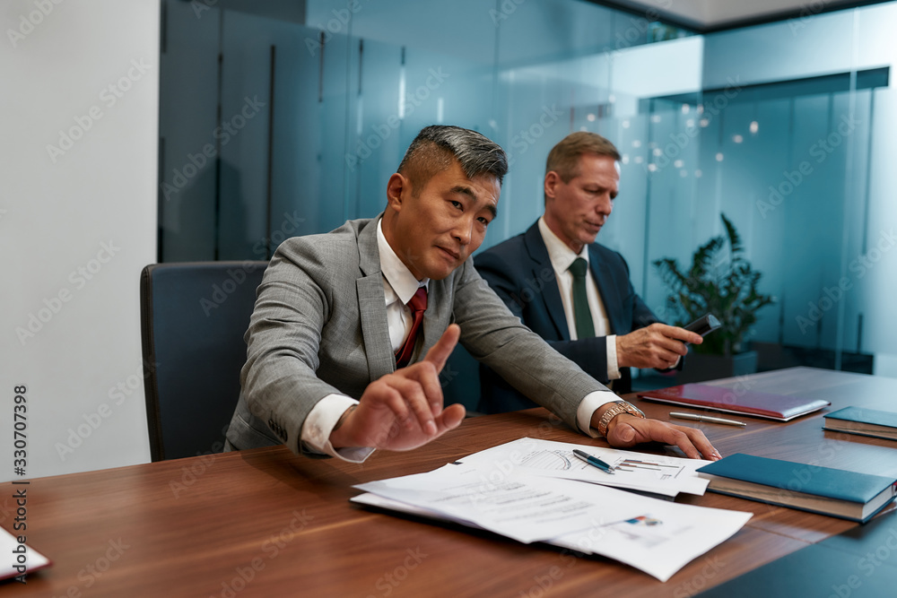 Stop. Asian businessman in formal wear don't want to sign contract while having a meeting with partners in the modern office Stop. Asian businessman in formal wear don't want to sign contract while having a meeting with partners in the modern office