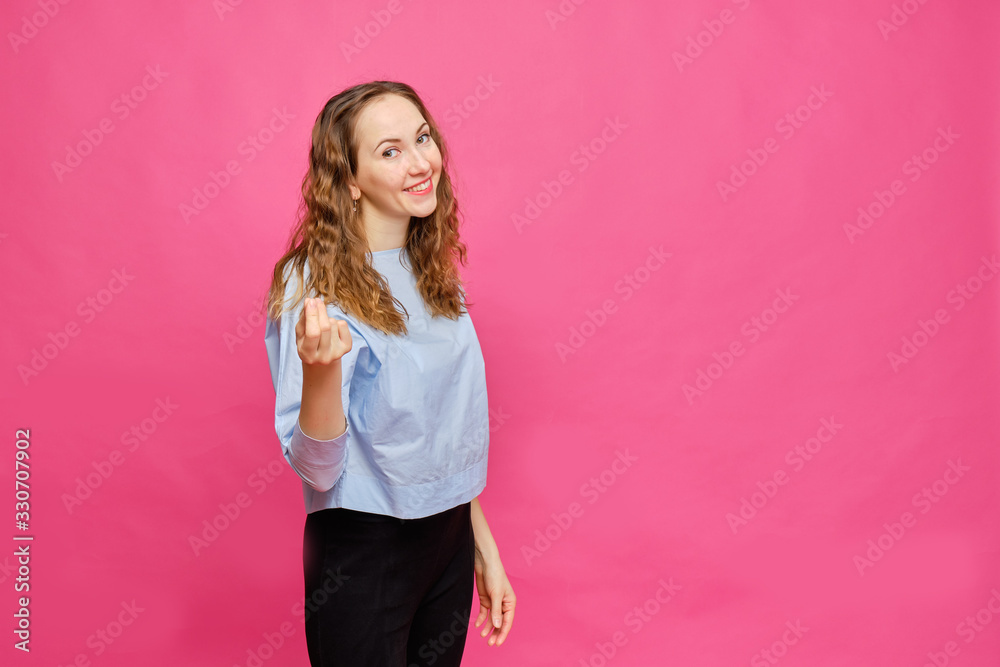 Stylish caucasian girl in a pale blue t-shirt shows an abstract money gesture on a pink background. Stylish caucasian girl in a pale blue t-shirt shows an abstract money gesture on a pink background.