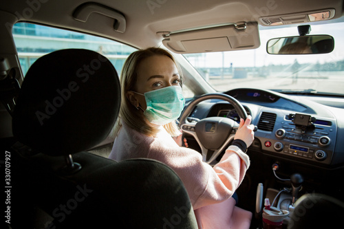 Woman in protective mask driving a car on road. Safe traveling. photo