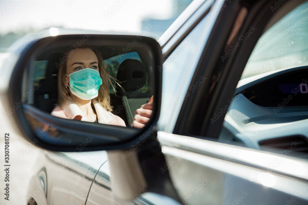 Woman in protective mask driving a car on road. Safe traveling. - obrazy, fototapety, plakaty 