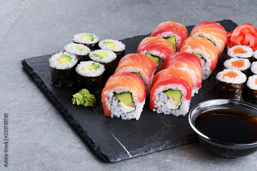 Sushi maki with salmon and avocado, sushi philadelphia, soy sauce and ginger on a background of slate board.