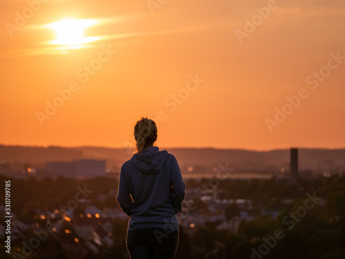 Rear view of woman enjoying beautiful sunset with the city of Augsburg in the background