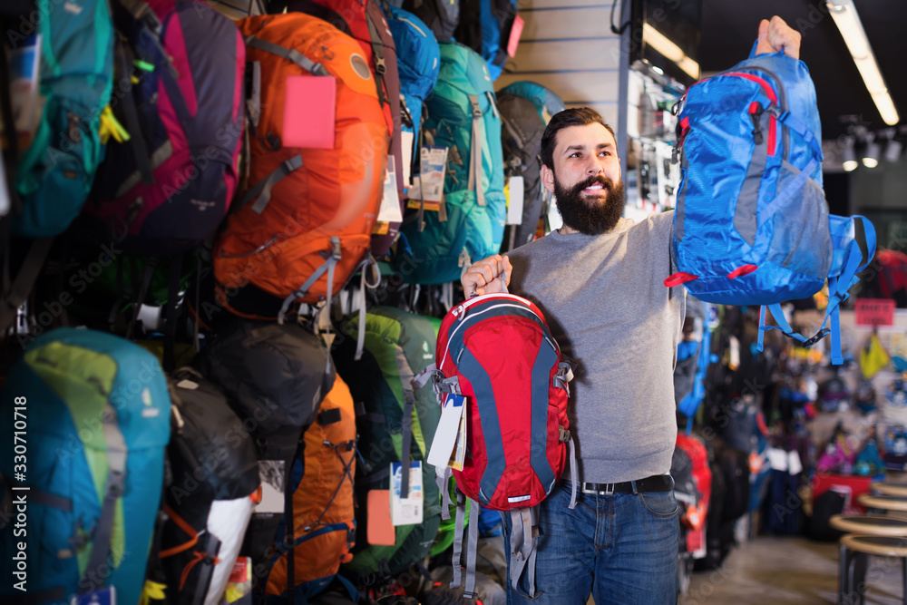 Smiling man customer examining rucksacks in store