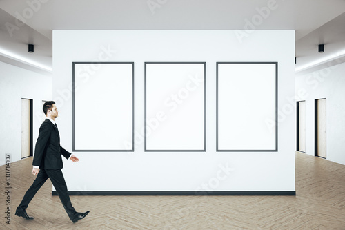 Businessman walking in modern hall interior with blank poster on wall