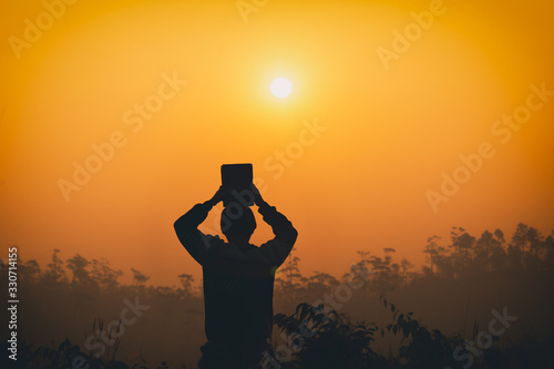 Human kneel down and lift Bible up on head with light sunset background, christian silhouette concept.