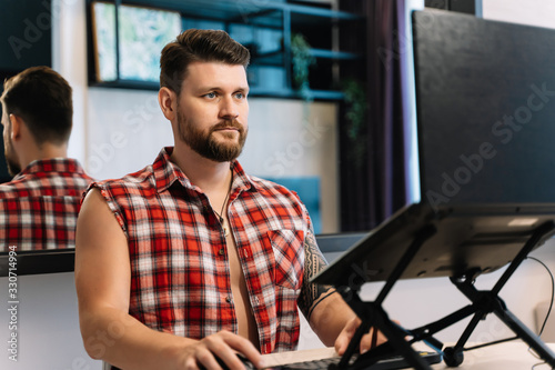 Photos Man with a beard and a plaid sleeveless shirt working remotely in front of a lap