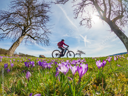 Obraz na plátne happy yound woman riding her electric mountain bike in a meadow with colorful bl
