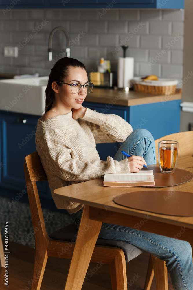 Woman drinking tea writing notes in notebook.