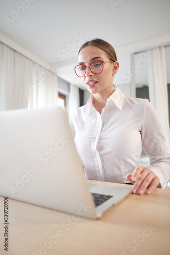 woman in eyeglasses sitting with computer on couch, looking outside, cannot concentrate on work, need some rest, feeling bored, need additional motivation, working remotely at home.