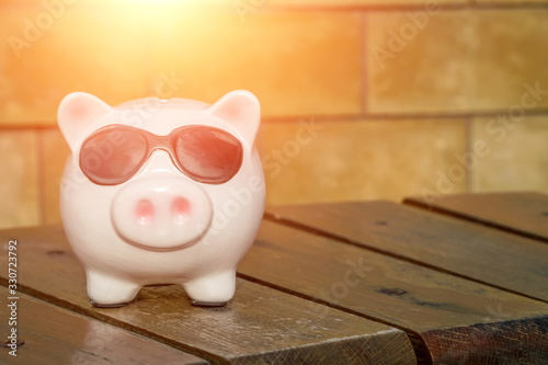 Piggy Bank in the form of a pink pig with black glasses on a wooden bench with copy space, photo with illumination
