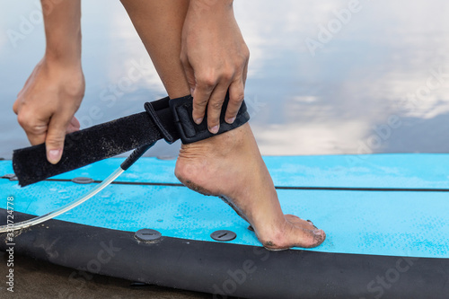 Woman is fastening surfing leash on her ankle