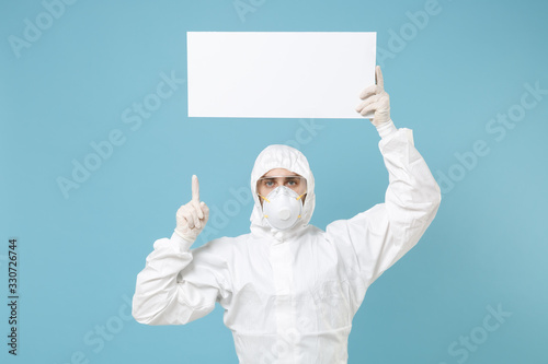 Man in protective suit respirator mask hold big white empty blank board place for text isolated on blue background studio. Epidemic rapidly spreading coronavirus 2019-ncov medicine flu virus concept. photo