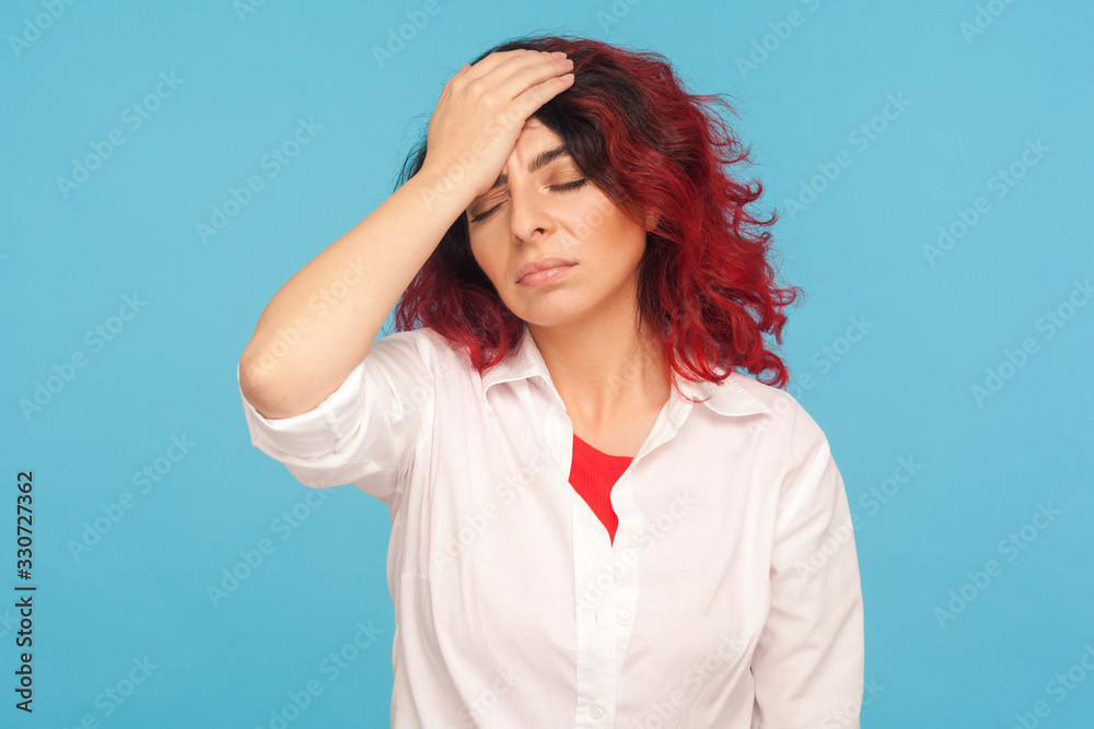 Portrait of upset woman with fancy red hair making facepalm gesture, feeling sorrow about forgotten event, holding aching head, worried about troubles. indoor studio shot isolated on blue background Portrait of upset woman with fancy red hair making facepalm gesture, feeling sorrow about forgotten event, holding aching head, worried about troubles. indoor studio shot isolated on blue background