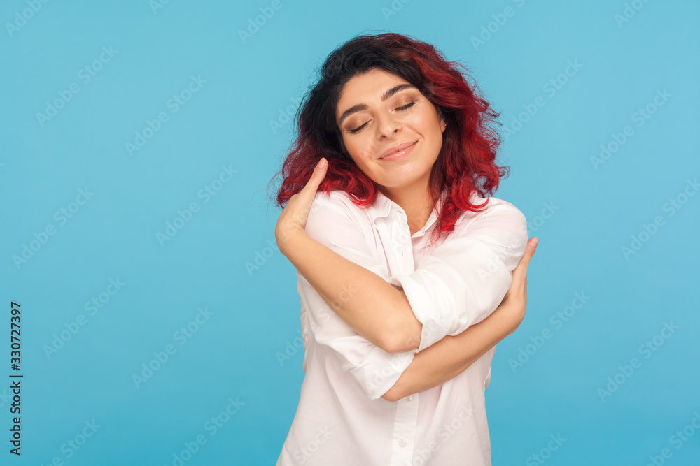 I love myself. Portrait of beautiful narcissistic woman with fancy red hair embracing herself with pleased satisfied face expression, positive self-esteem. studio shot isolated on blue background I love myself. Portrait of beautiful narcissistic woman with fancy red hair embracing herself with pleased satisfied face expression, positive self-esteem. studio shot isolated on blue background