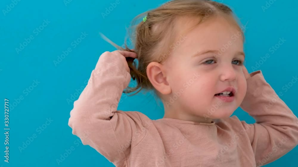 Cute little girl with beautiful big blue eyes points her ponytails and looking at camera isolated on blue background Cute little girl with beautiful big blue eyes points her ponytails and looking at camera isolated on blue background