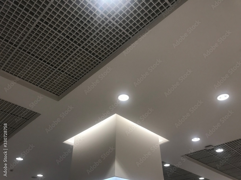 Suspended Grid false ceiling with gypsum bulkhead design and column coves  with indirect lighting for a lucrative design view for a shopping mall and  emulsion painted ceiling which has down lights Stock