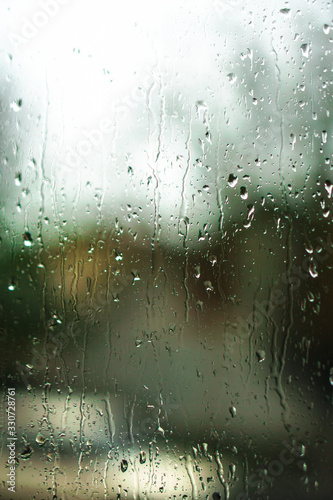 Window overlooking a rainy street. Gloomy evening weather with a view of the road. Drops on glass and bokeh from cars. Stock background for design