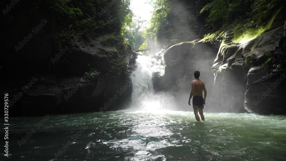 Happy man standing in front of a waterfall feeling free and takes a breathe.