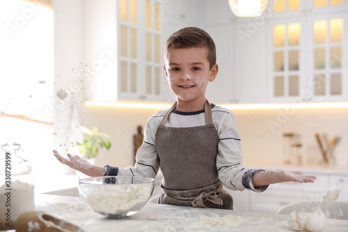 Cute little boy cooking dough at table in kitchen