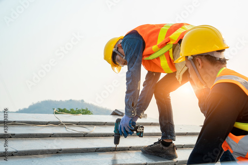 Roofer worker in protective uniform wear and gloves,Using air or pneumatic nail gun and installing concrete roof tile on top of the new roof,Concept of residential building under construction.